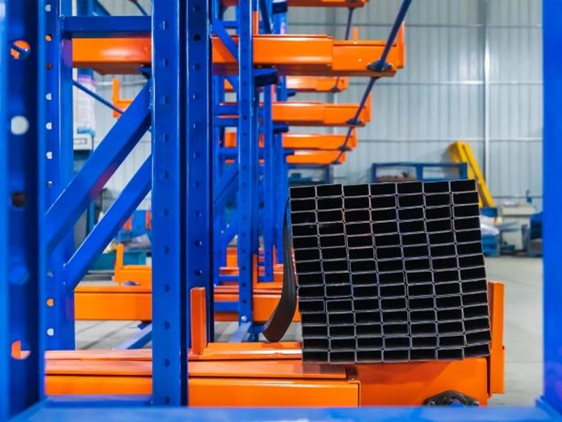Warehouse telescopic cantilever rack with blue uprights and orange arms storing rectangular steel tubes