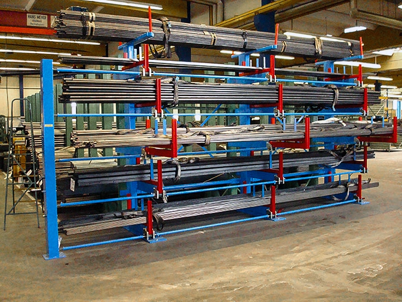 Heavy-duty telescopic cantilever rack holding long steel profiles in a busy fabrication warehouse