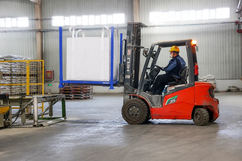 Forklift operator transporting heavy duty demountable steel post pallet with a bulk bag in warehouse.