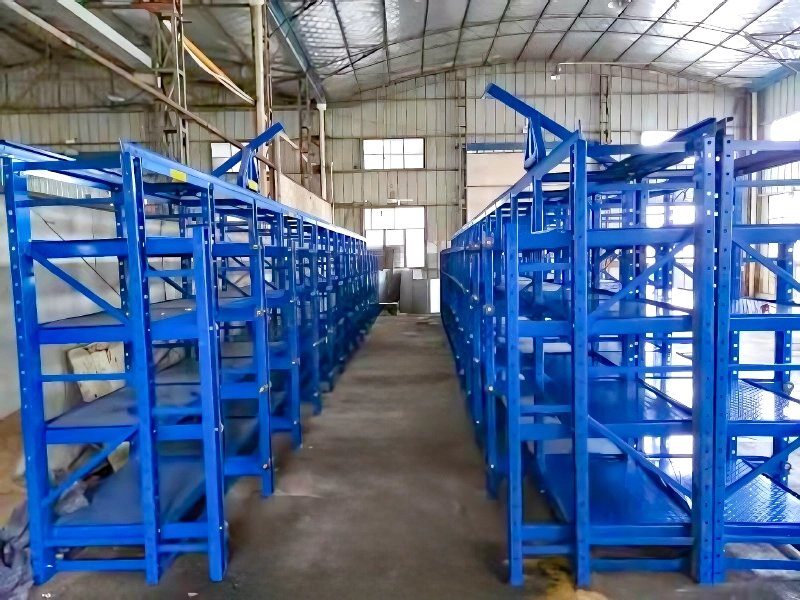 Blue roll-out mold racks with steel drawer frames and overhead crane access in a workshop aisle