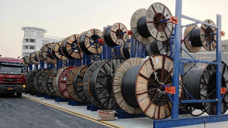 Outdoor cable reel storage racking system on concrete site next to asphalt road with a red logistics transport truck