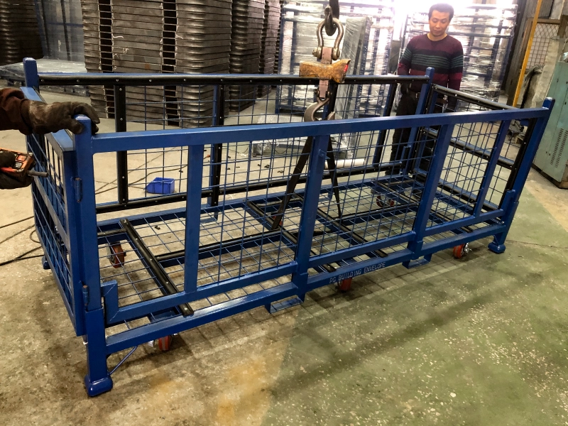 Langwerpige blauwe draadcontainer wordt opgetild door bovenloopkraan in fabriek