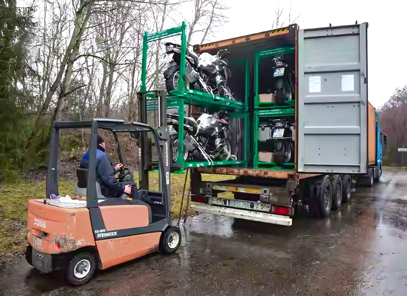 Forklift loading green steel motorcycle shipping pallet rack into export container with stacked double-tier frames