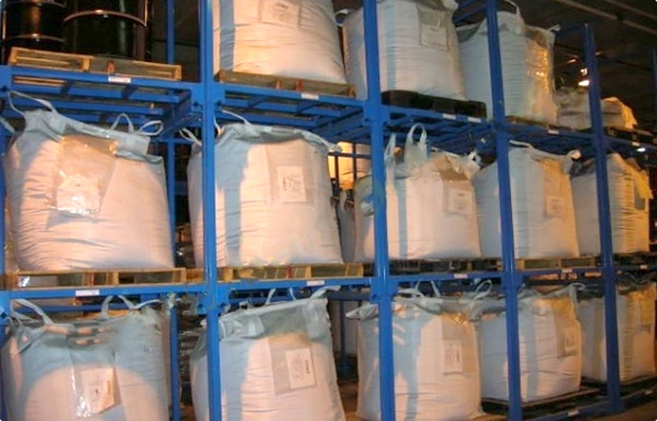 Three tier stacked blue steel nestainer racks storing large white FIBC bulk bags on wooden pallets in warehouse