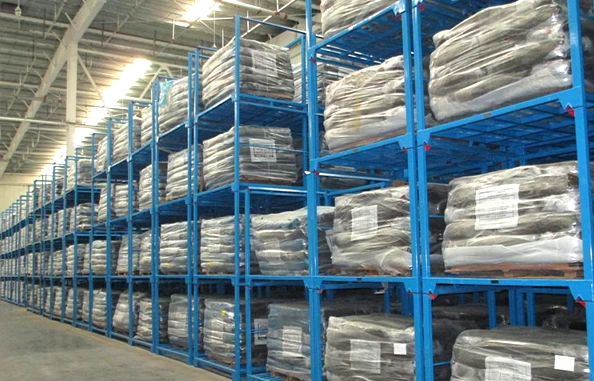 Four tier stacked blue steel nestainer racks containing stretch wrapped palletized goods in a large industrial warehouse