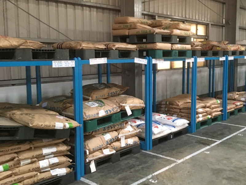 Real warehouse photo of blue steel stack racks supporting palletized bagged goods for vertical storage