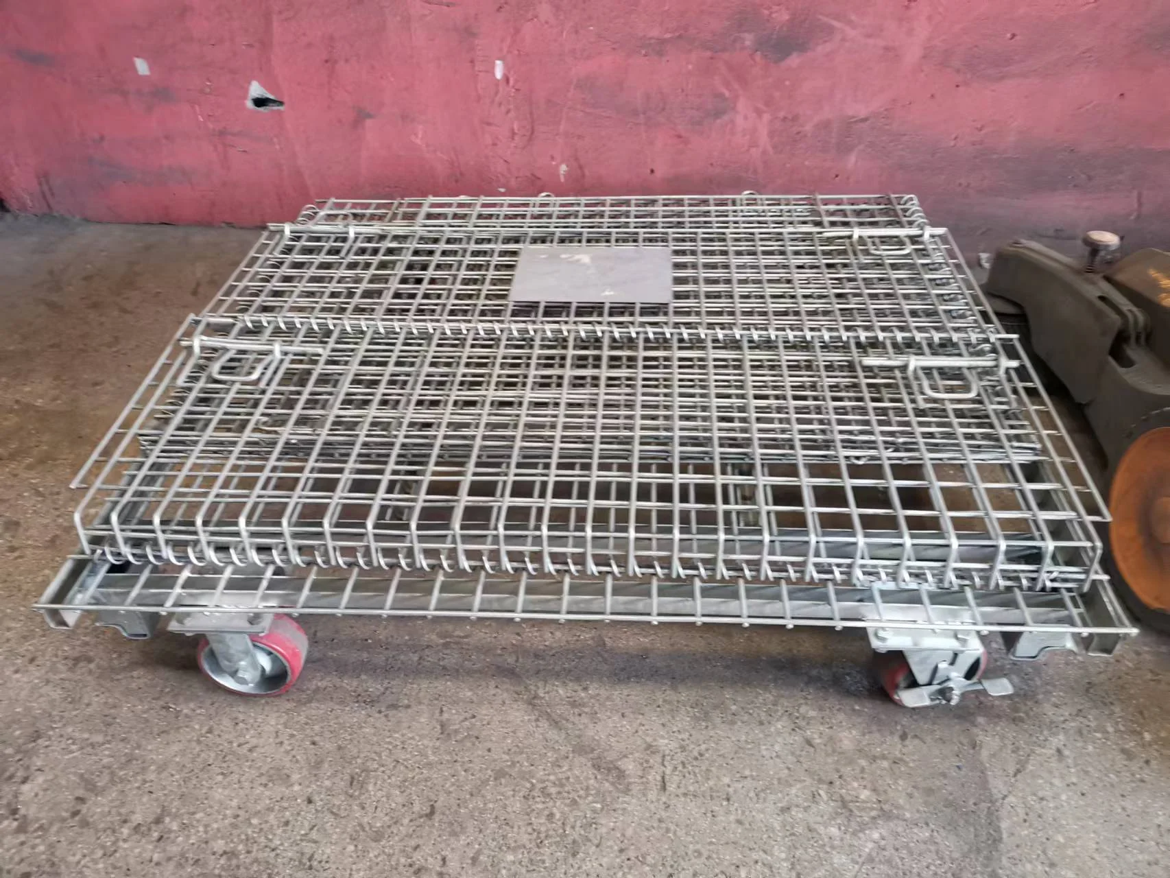Folded rolling wire mesh container showing red polyurethane wheels welded to the steel base.
